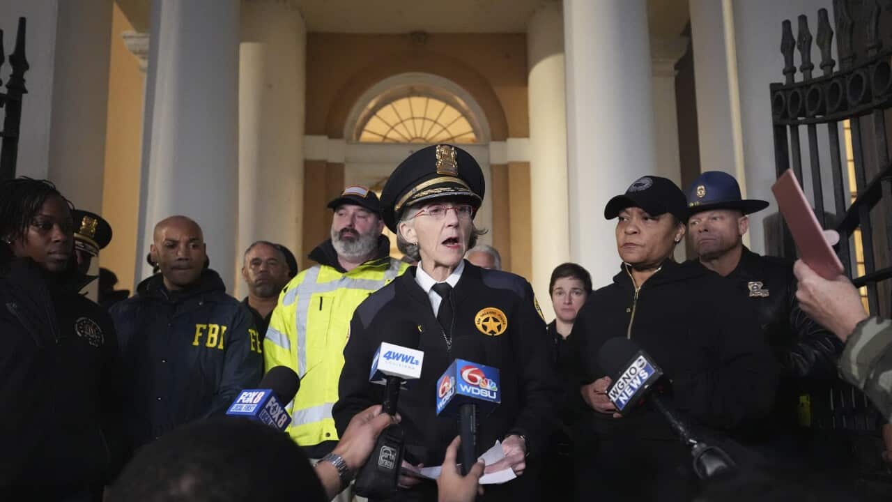 A police officer speaks at a press conference surrounded by other officials and journalists.