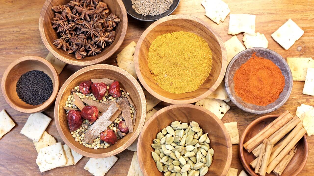 Spice blend featuring star anise, curry, paprika, chili peppers scattered near crisp crackers on rustic wooden background, highlighting vibrant culinary palette