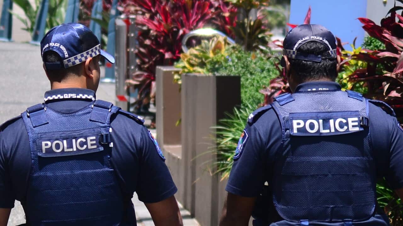 Rear view of two police officers in blue uniforms and wearing blue caps walking down a street.