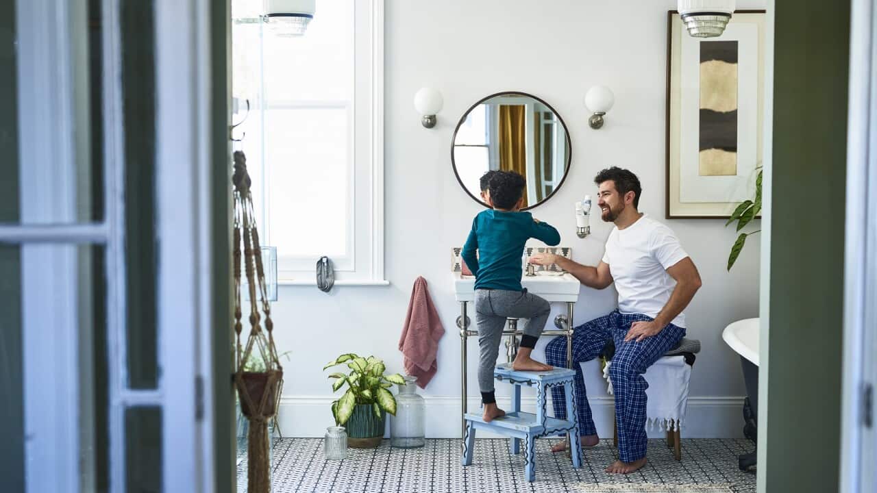 Father helping son brushing teeth in bathroom