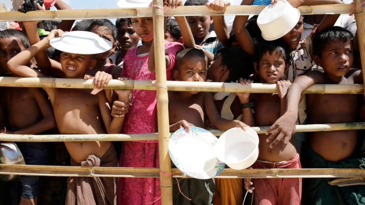 Rohingya children stand behind a bamboo fence and wait to get into the queue to collect lunch time food center in a camp.