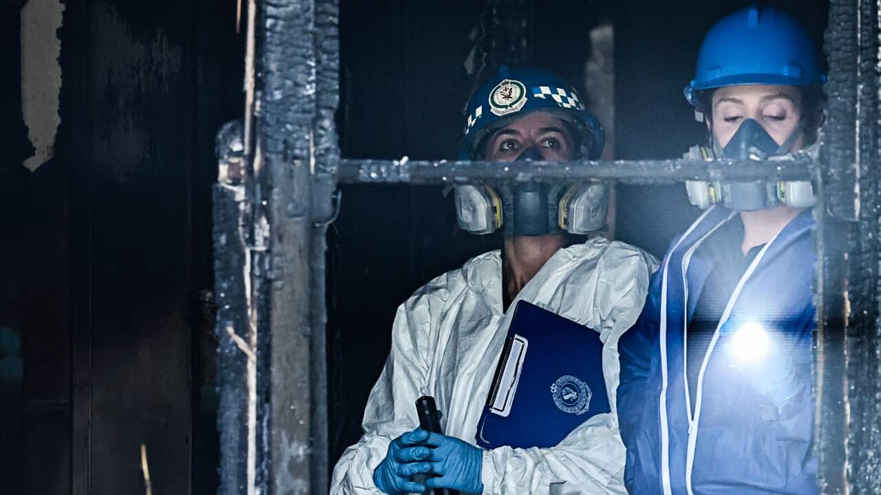 Two women wearing face masks inspect a building that has been damaged by fire.