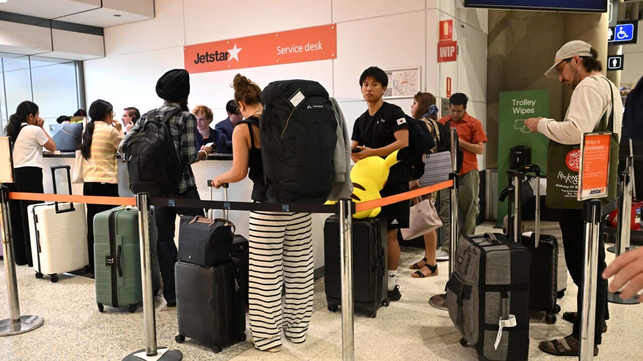 Passengers queue with luggage at a Jetstar service desk inside an airport.