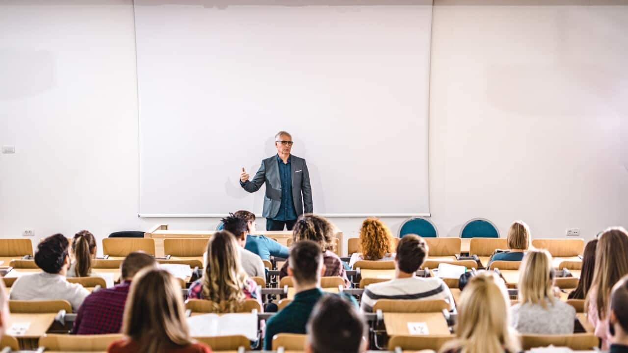 Senior teacher talking to large group of college students in amphitheater.