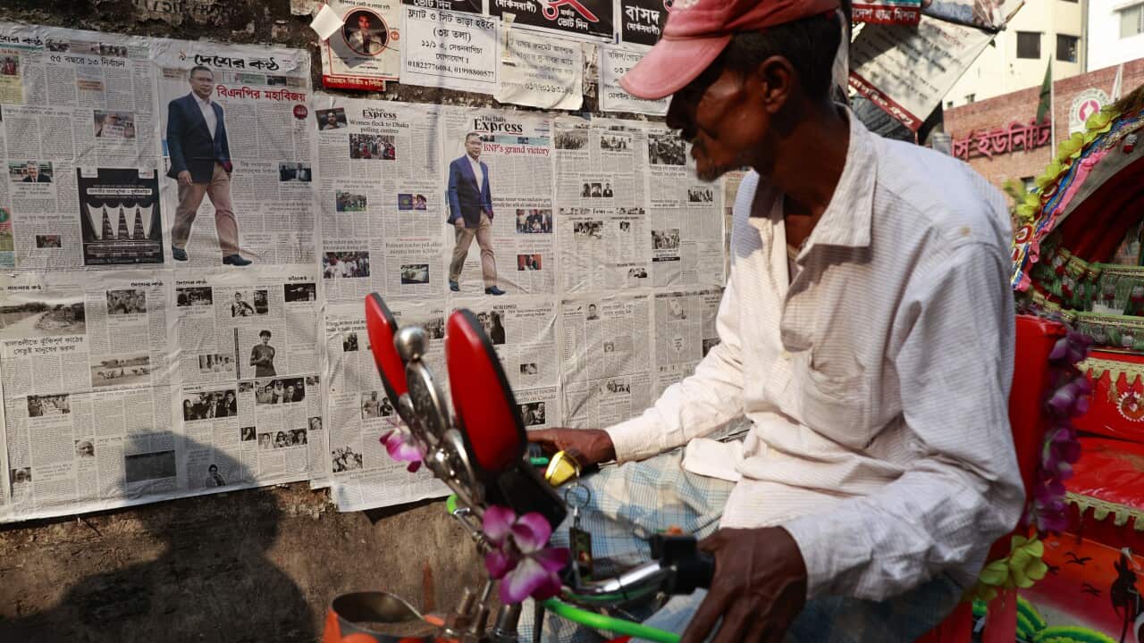 A man on a bike reads a newspaper pasted on a roadside wall.