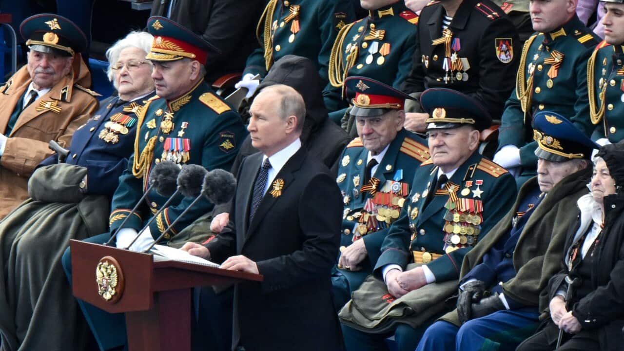 A man stands at a lectern with several mean and woman in military dress seated behind him