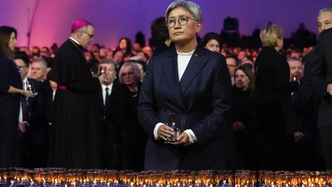Penny Wong standing in front of a row of candles. A large group of people are seated behind her.