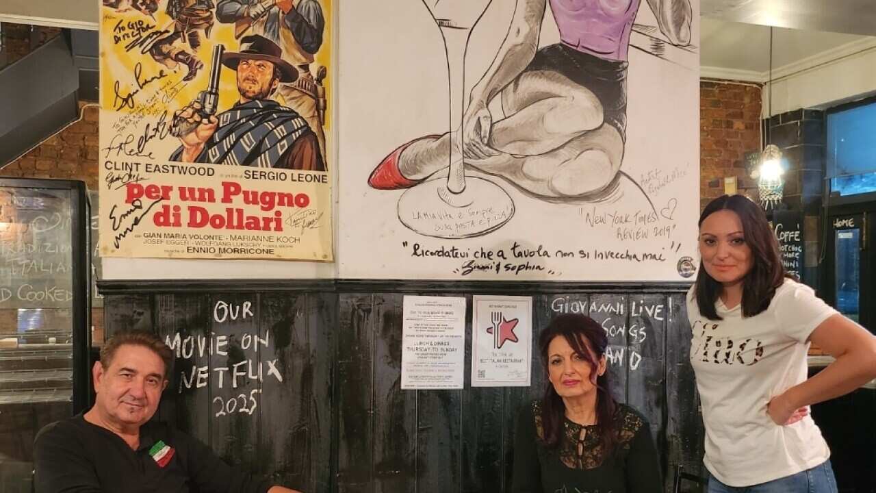 A man and a woman sitting at a restaurant table and another woman standing beside