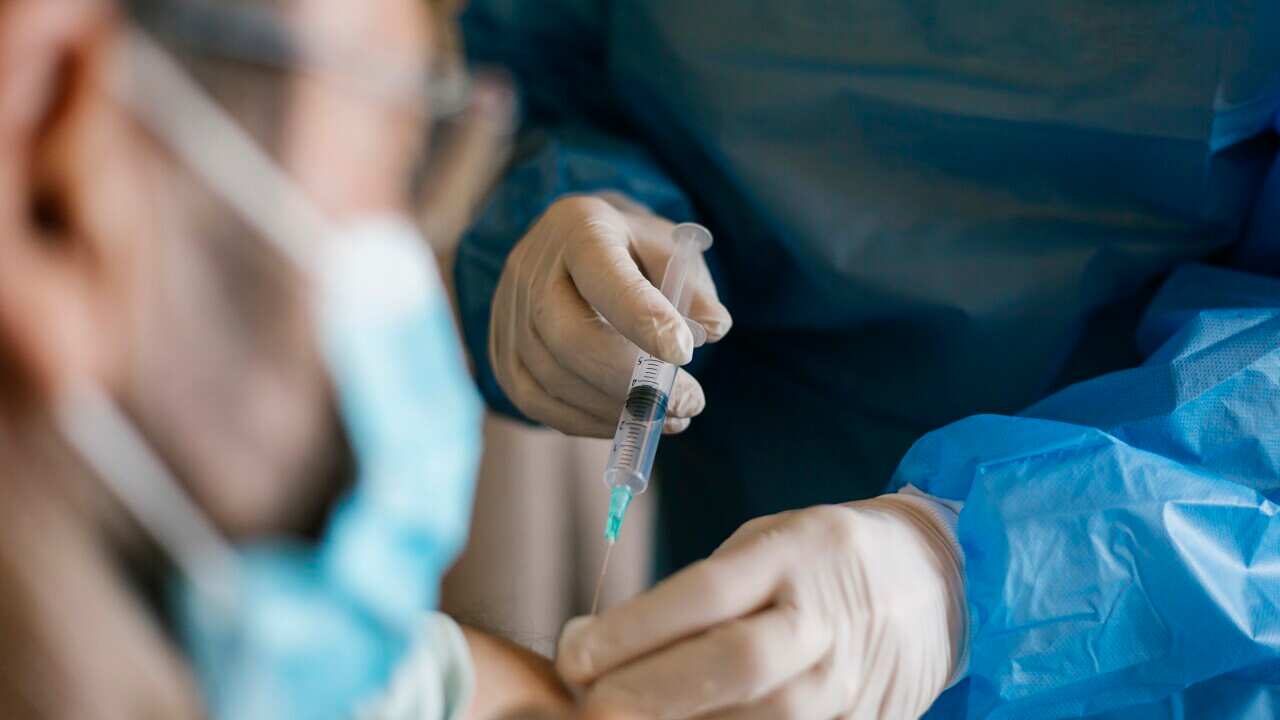 A close up photo of a person wearing surgical gloves and scrubs injecting a syringe into a person's arm.