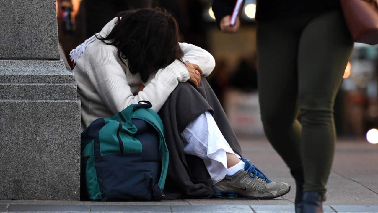 A homeless woman sits on a street corner
