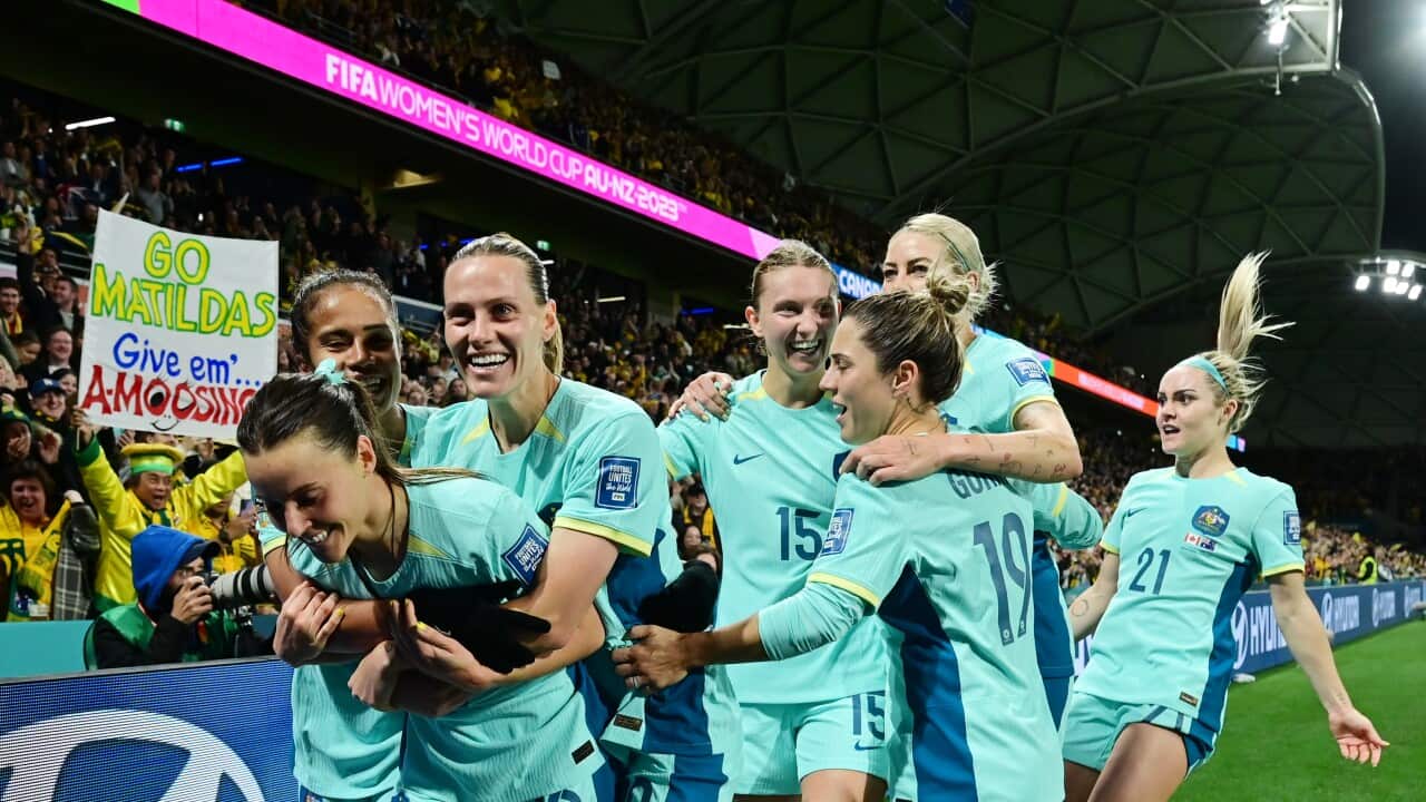 Matildas players cheering and hugging on a stadium field.