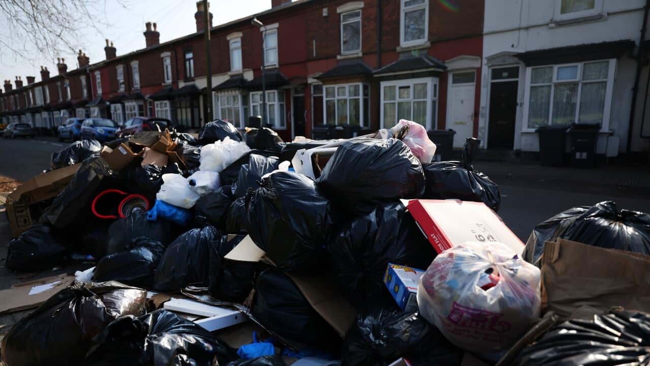 A pile of rubbish bags in front of a row of residential dwellings.