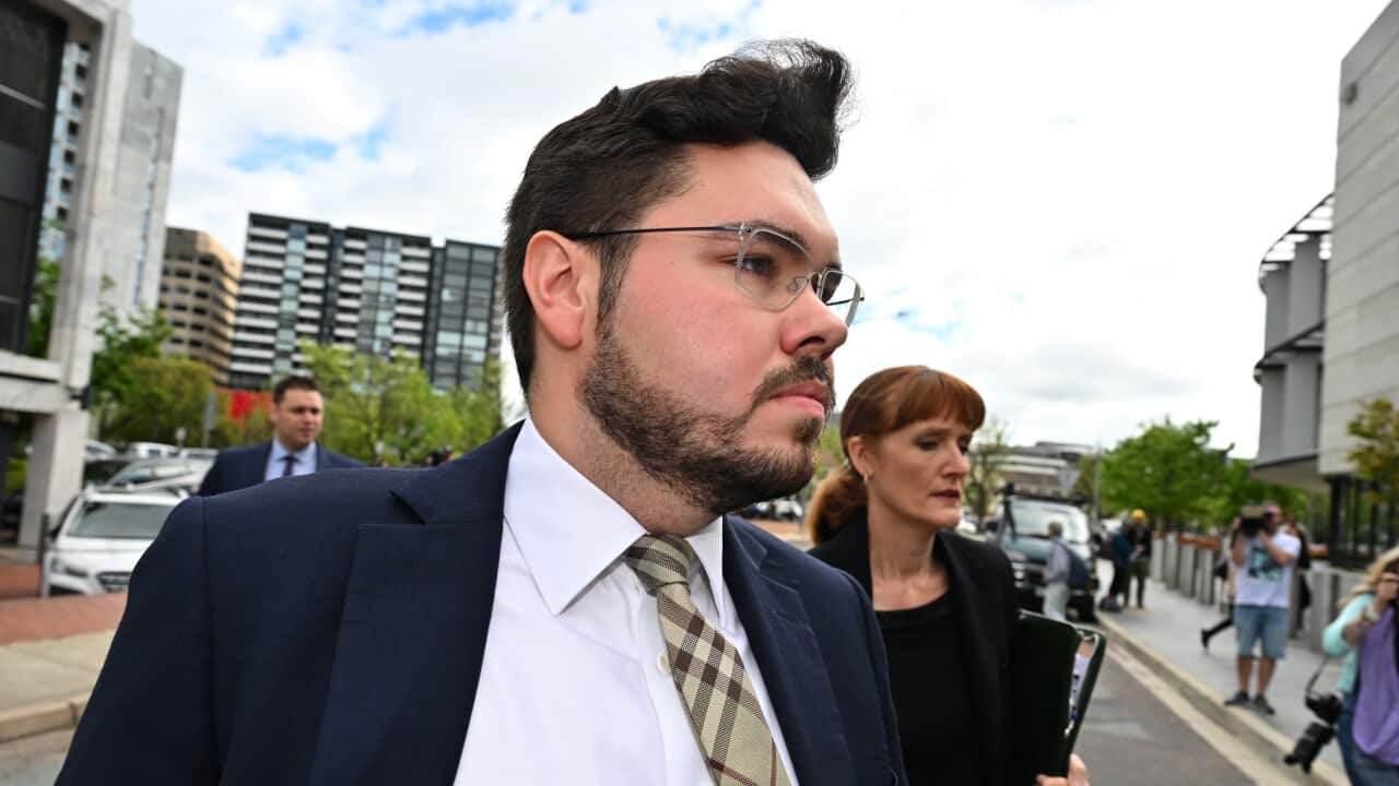 A man wearing a suit, tie and glasses who is walking outside.