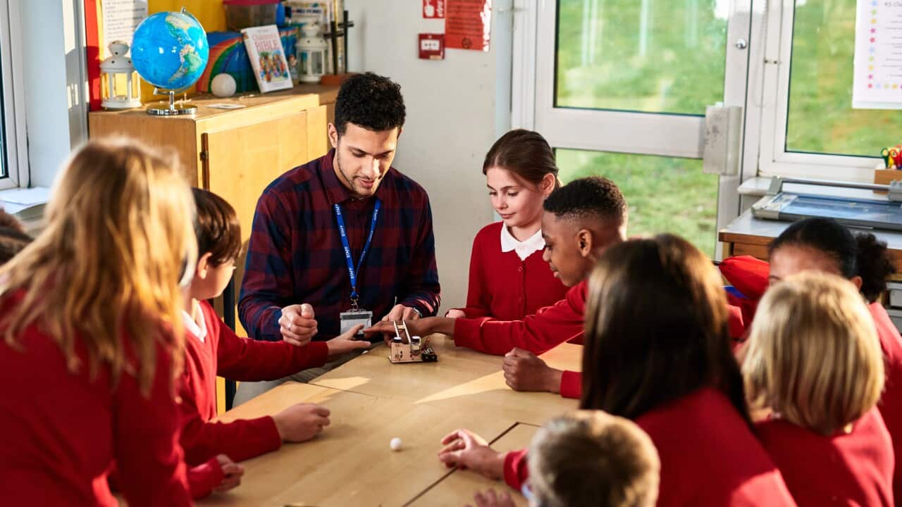 Male teaching assistant explaining to primary school children in Design Technology class