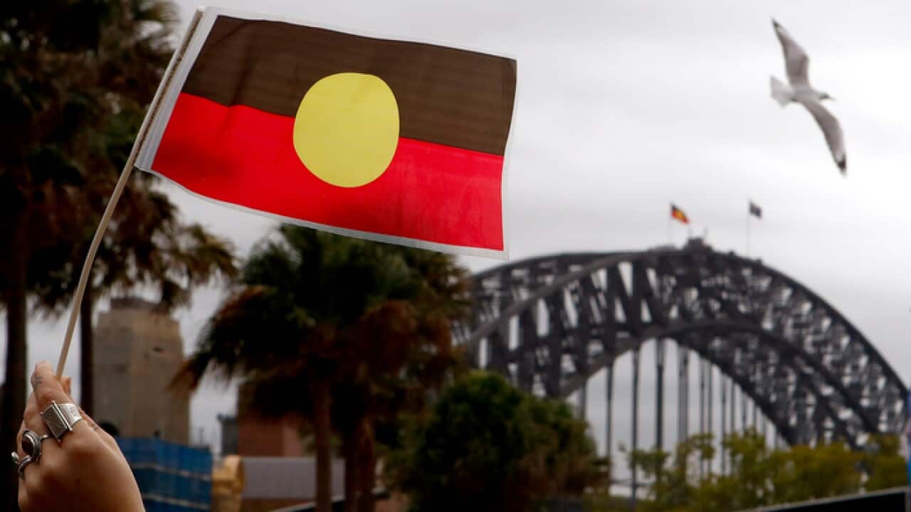 A woman holds an Australian Aboriginal Flag during a demonstration in Sydney, Saturday, June 2, 2018. The demonstrators are calling for the Australian Aboriginal Flag to be flown atop Sydney Harbour Bridge. (AAP Image/Daniel Munoz) NO ARCHIVING