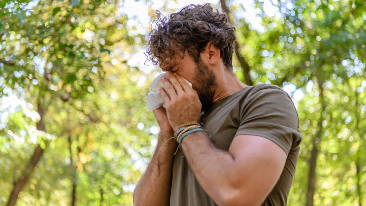 A man sneezing with trees in the background.