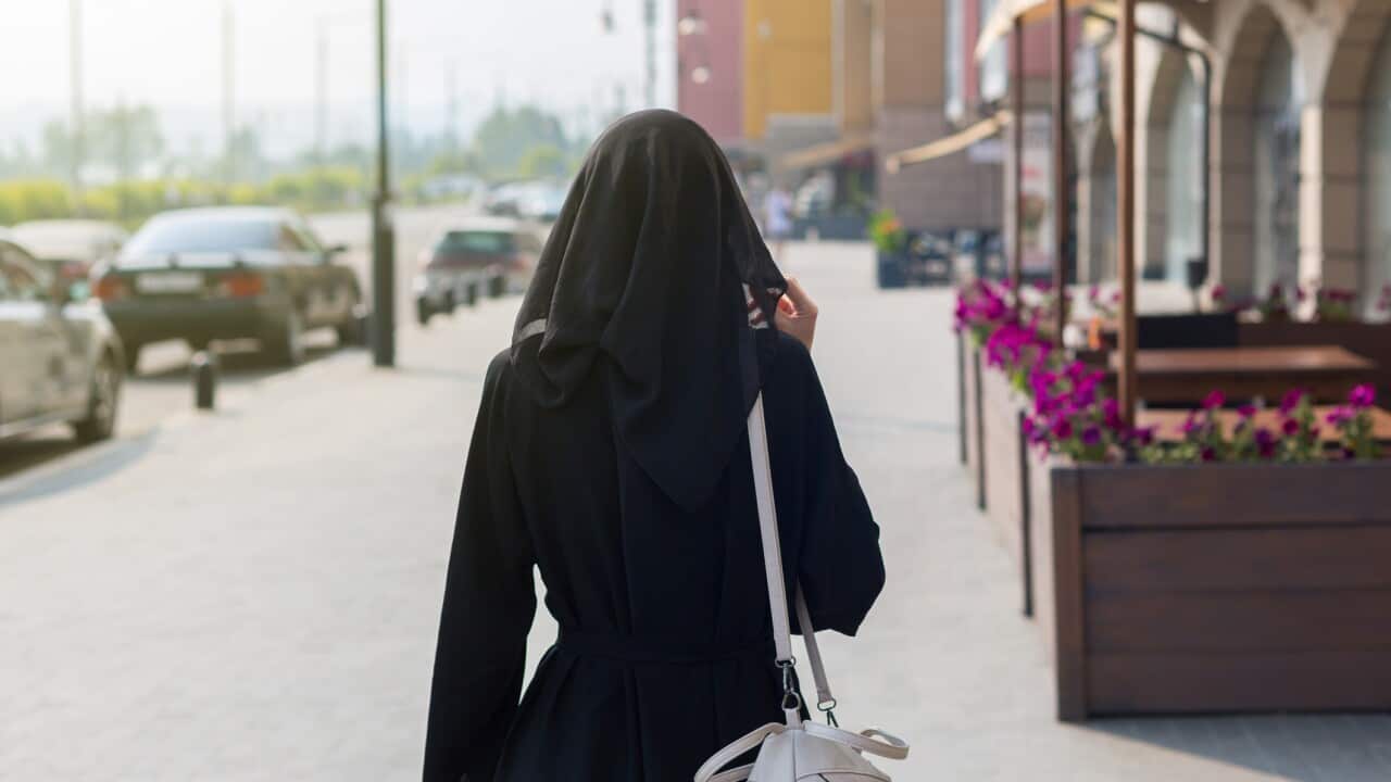 A single Muslim woman walks through empty big city rear view.