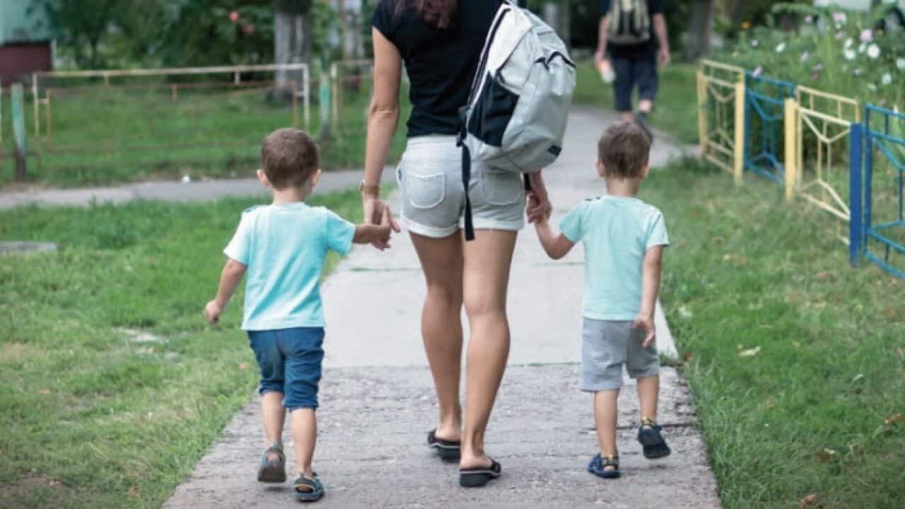 An au pair walks between two children