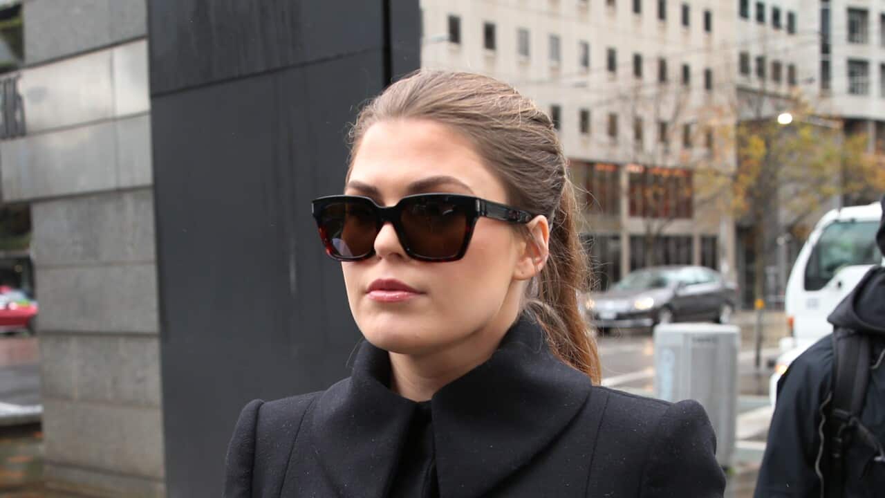 A woman wearing all black and a pair of sunglasses outside a courthouse.