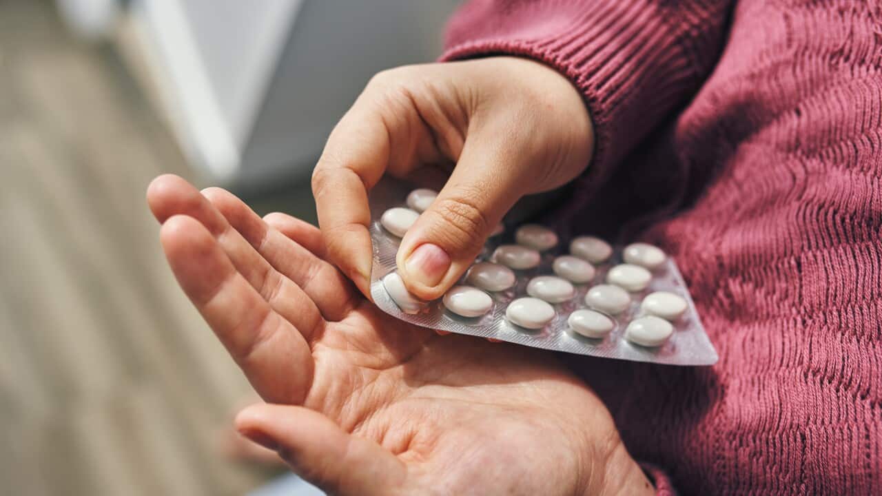 A person's hands popping white pills out of a blister pack.
