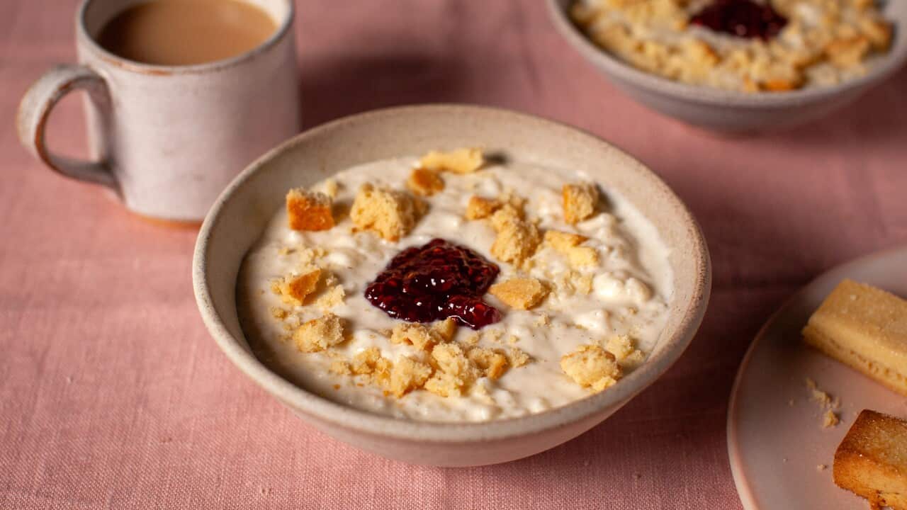 A bowl of rice pudding, topped with a dollop of jam and crumbled shortbread fingers.