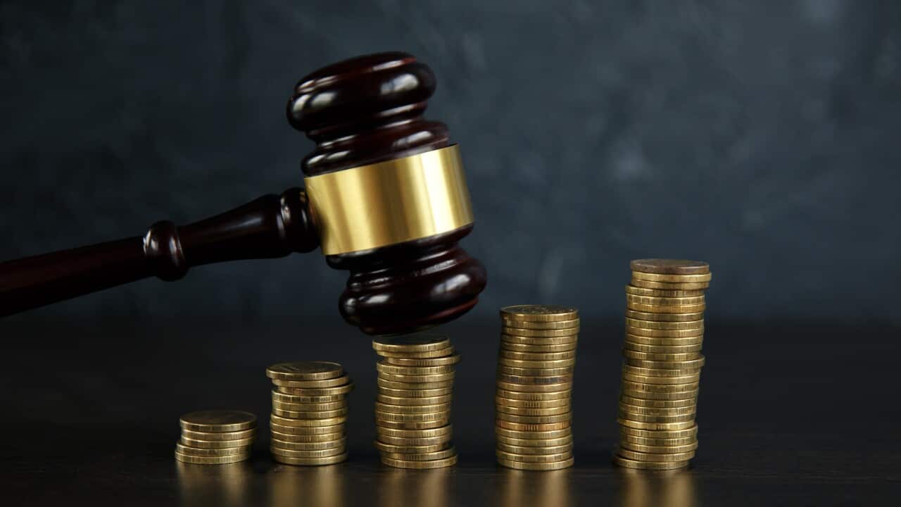 Close-up Of A Judge's Hand Holding Gavel Over Stacked Golden
