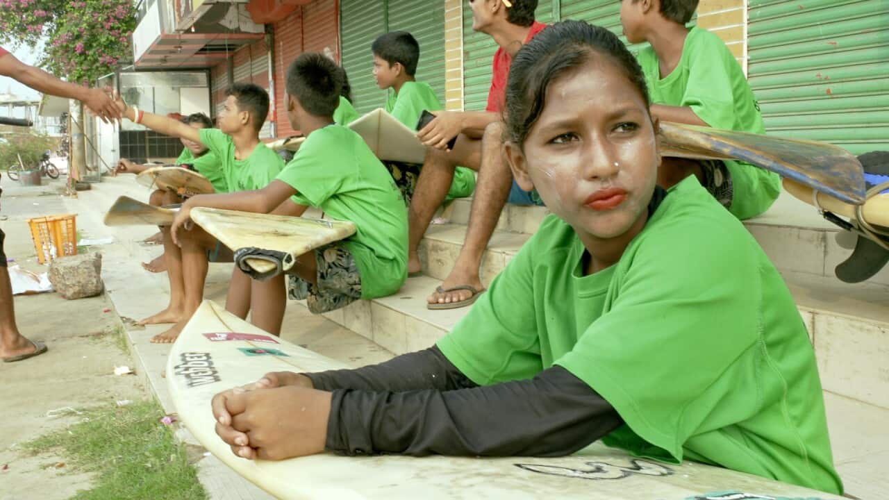 A girl sits with her surfboard.