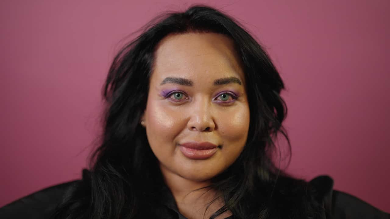 a headshot of a woman with green eyes smiling with a purple back drop