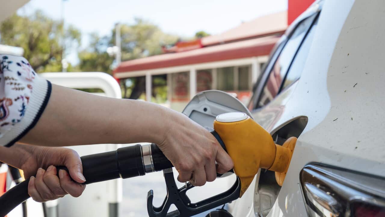 A woman's hand holds the petrol pump as she fills up her car