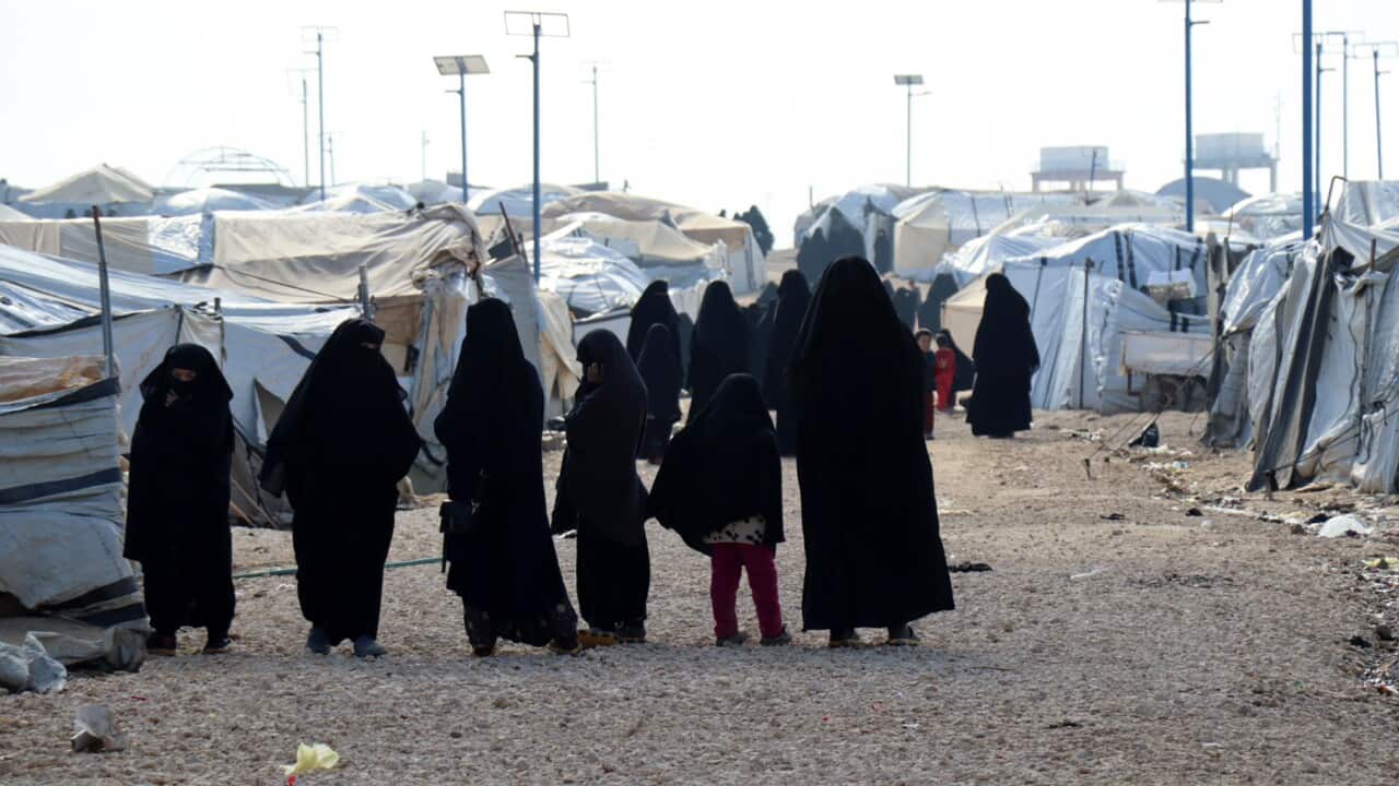 A row of women and children wearing black outfits standing amid tents