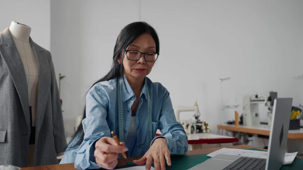 aged-asian-woman-tailor-working-in-fashion-atelier-lady-with-laptop-in-studio-professi-SBI-351142528.jpg
