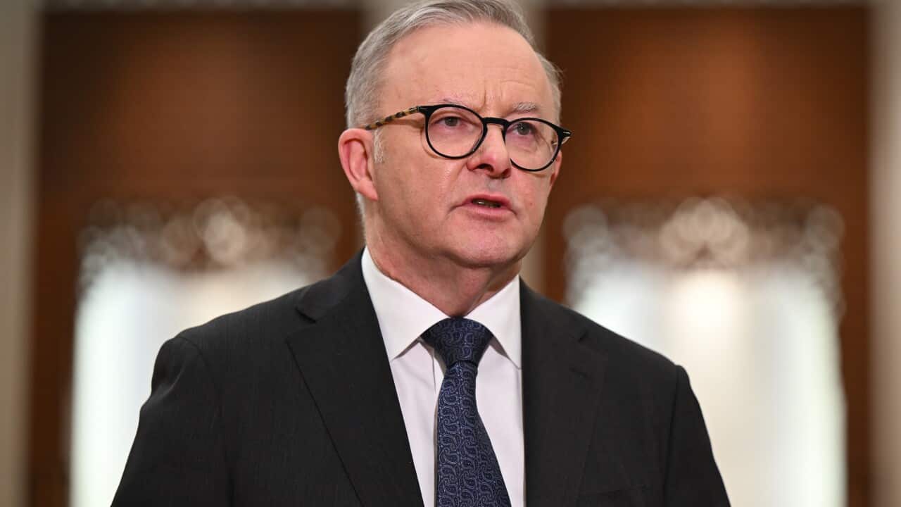 A man wearing a suit, tie and glasses who is speaking.