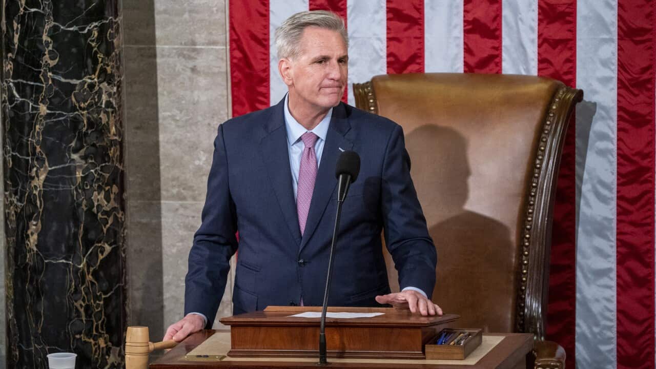 A man in a suit takes a gavel in his hand, with an American flag behind him.