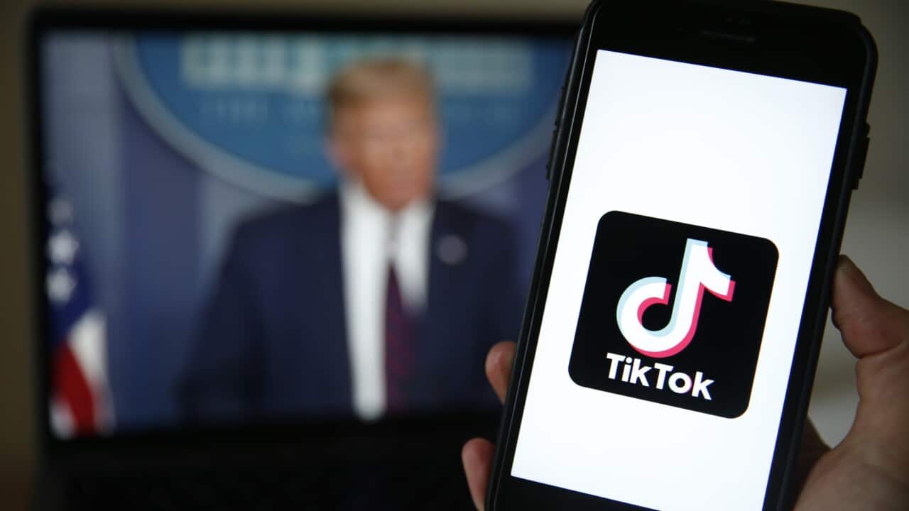 A phone displays the TikTok logo in front of a laptop showing a blurred image of Donald Trump.