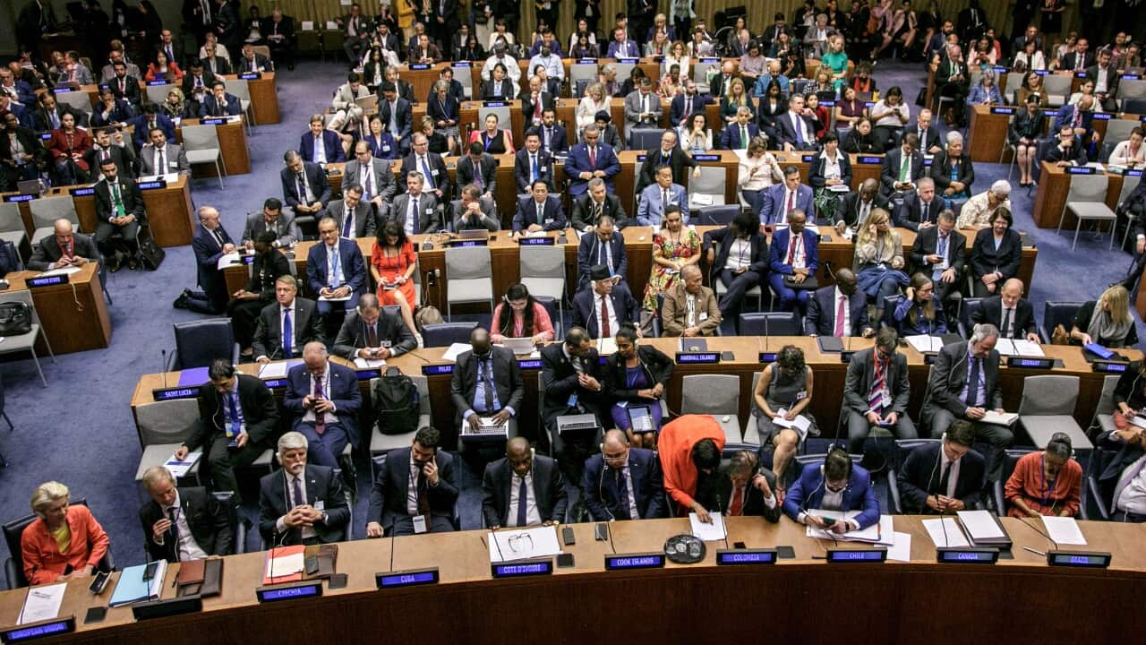 An overhead shot of a group of formally dressed people sitting at desks in a grand auditorium