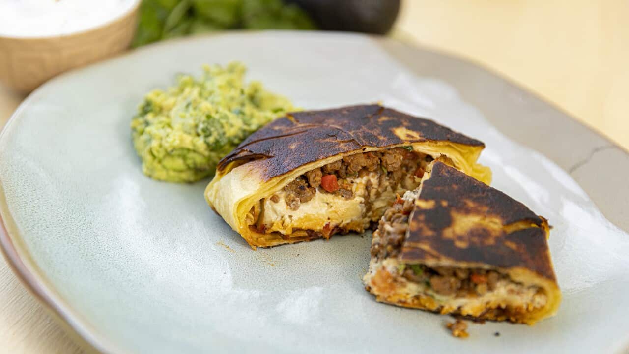 A round cooked tortilla parcel, cut open to show the filling, sit on a wide plate, along with a small mound of guacamole.