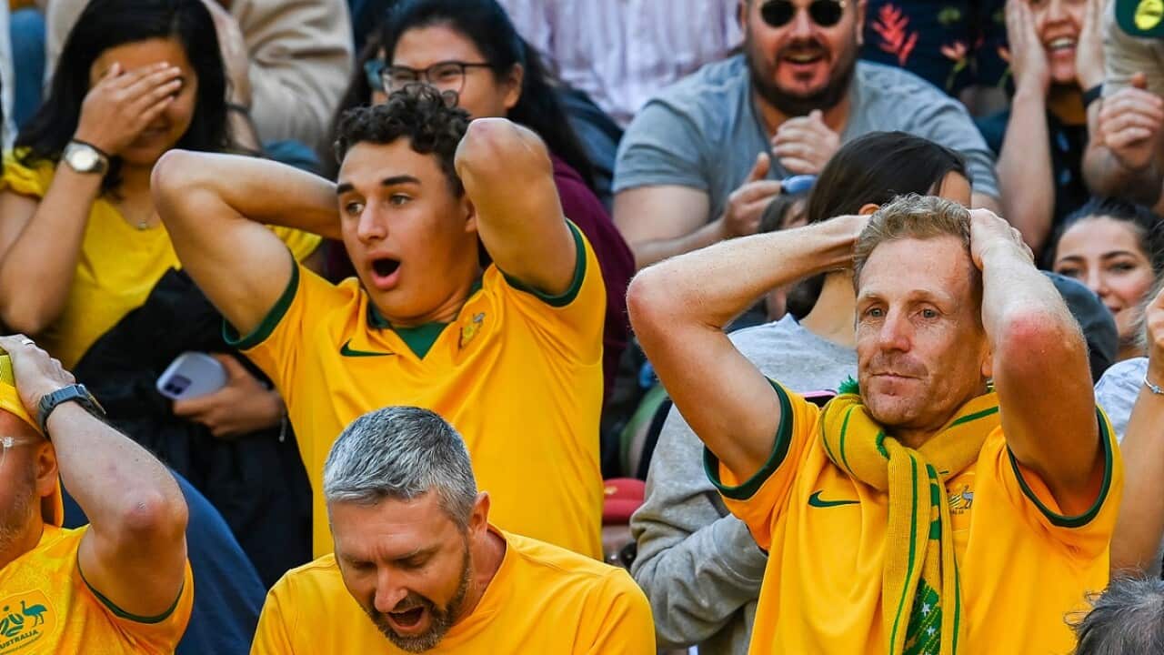 Several Sooceroos fans hold their hands on their heads in a crowd in Melbourne