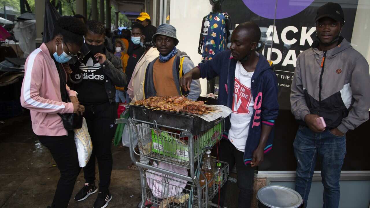 A woman wearing a face mask buys chicken on a crowded sidewalk in Pretoria.