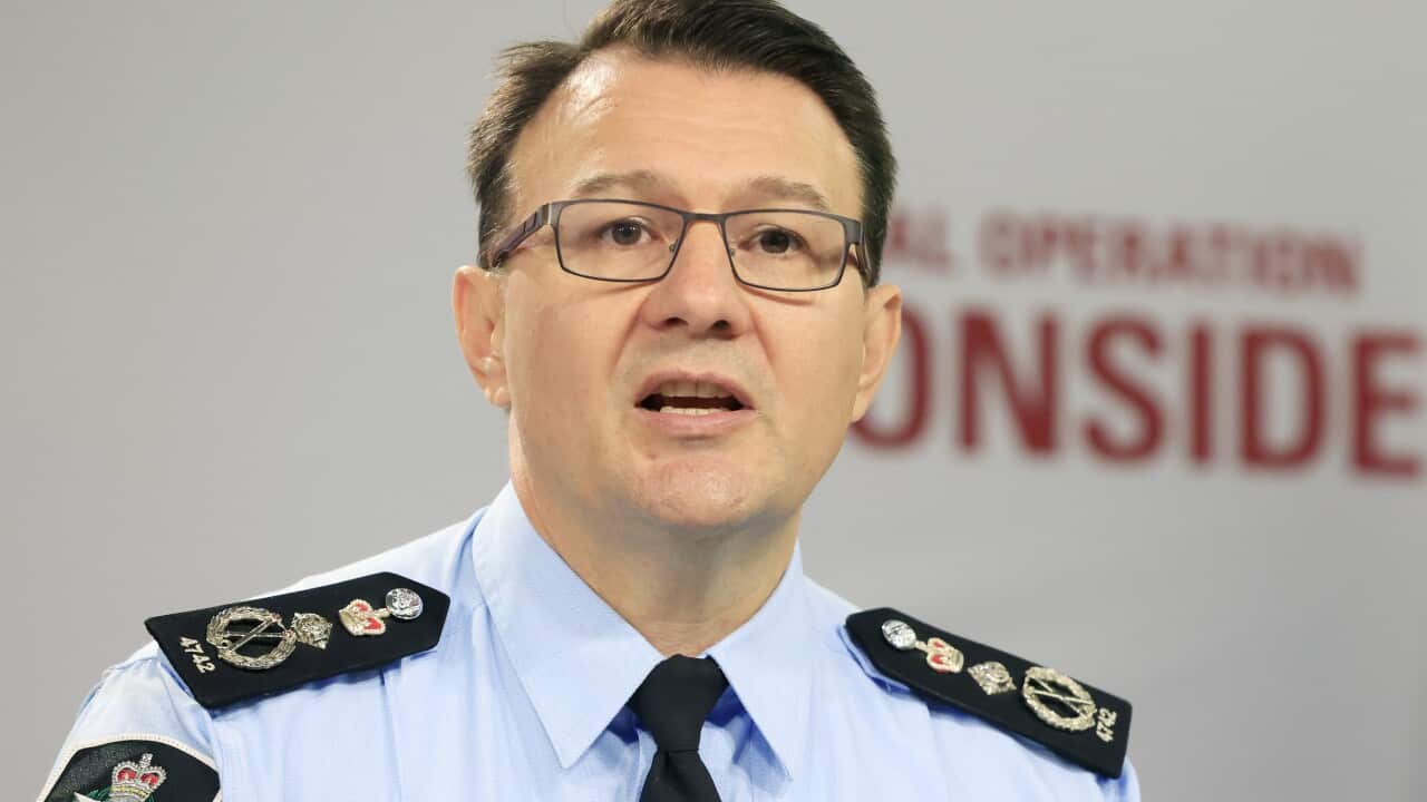 A man wearing glasses and the uniform of the Australian Federal Police speaks into a microphone.