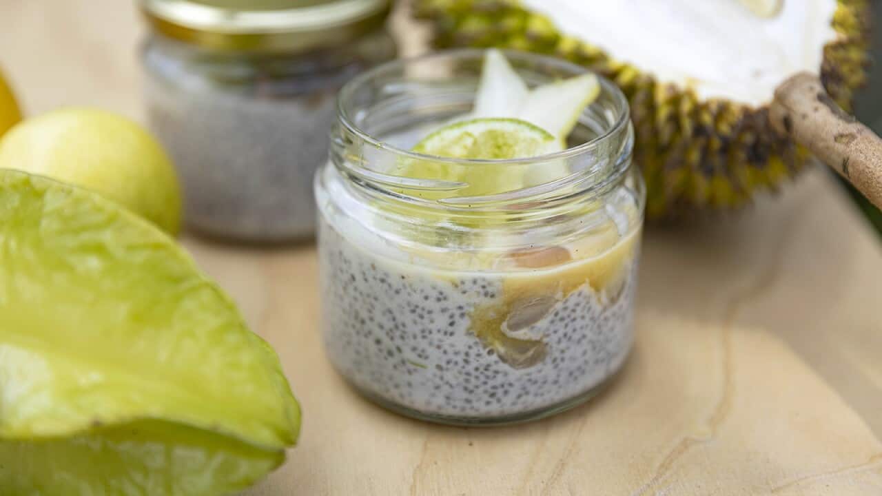 A jar with a chic mix topped with fruit sits on a cream surface. Another filled jar sites behind it, alongside various pieces of fresh fruit.
