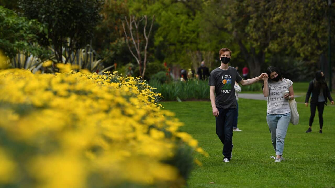 People wearing face masks hold hands while walking through Carlton Gardens in Melbourne, Saturday, September 11, 2021