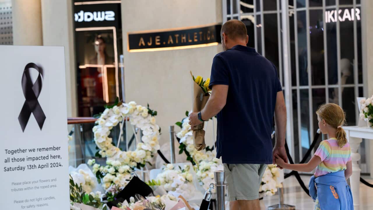 A man and a young girl approach a pile of floral tributes in a shopping centre.
