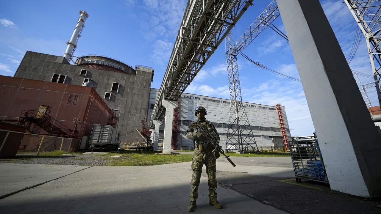 An armed soldier stands in front of large industrial buildings.