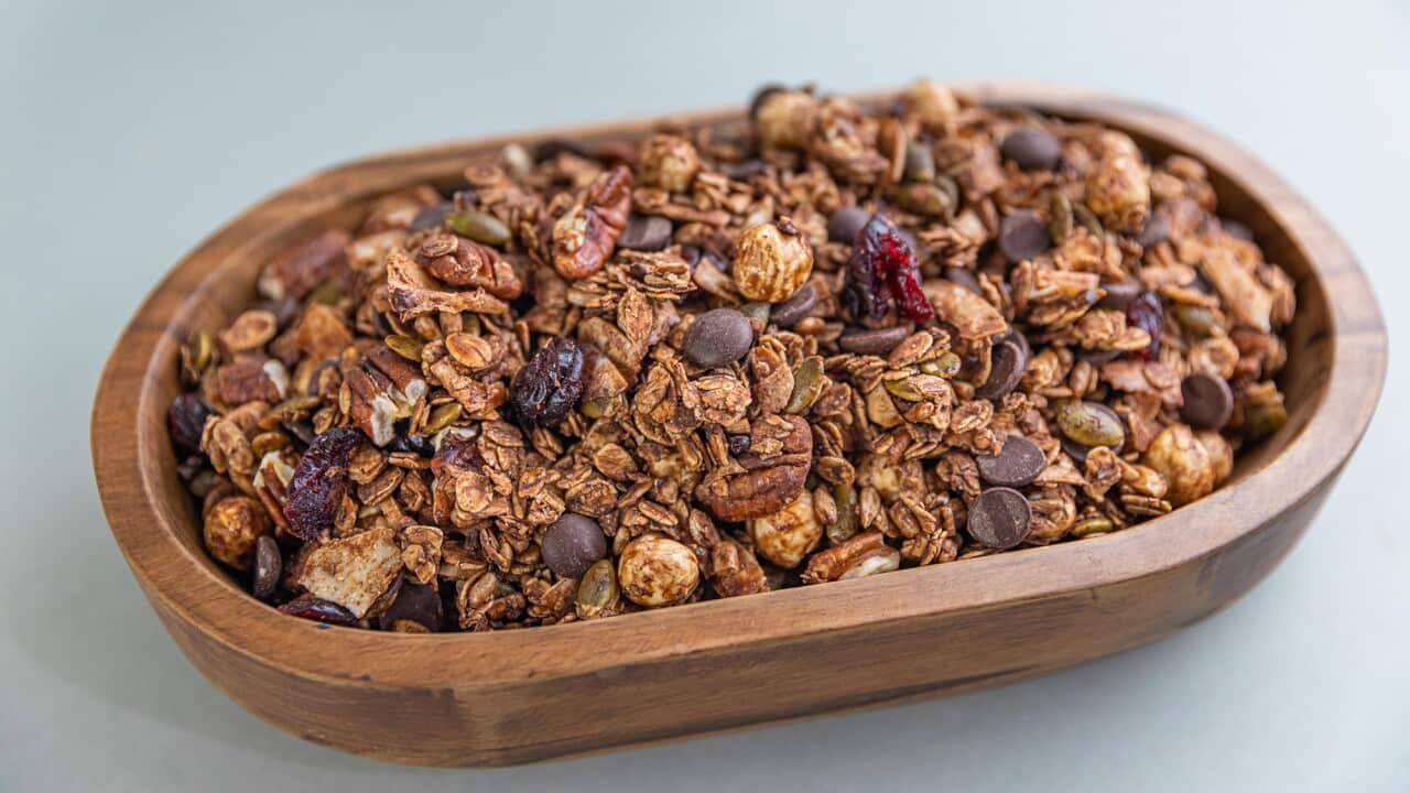 Toasted granola studded with cranberries and choc chips sit in an oval wooden bowl.