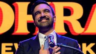 A man wearing a suit placed his hand on his chest while speaking to a microphone
