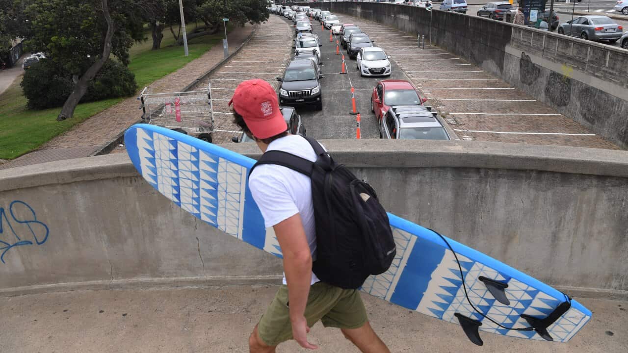 A surfer walks over a foot bridge as long lines of traffic wait to be tested for COVID-19 at the St Vincents Hospital drive-thru testing clinic in Bondi.