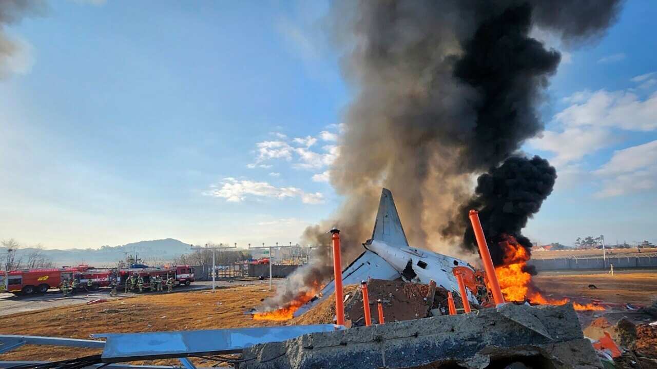 A thick plume of smoke rises from the wreckage of a plane at an airport.