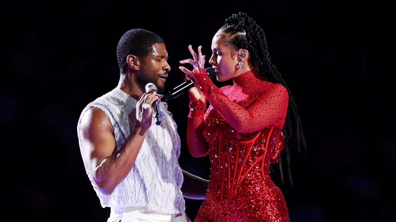 A man in a white sparkly outfit and a woman in a red sparkly outfit holding microphones and performing together.