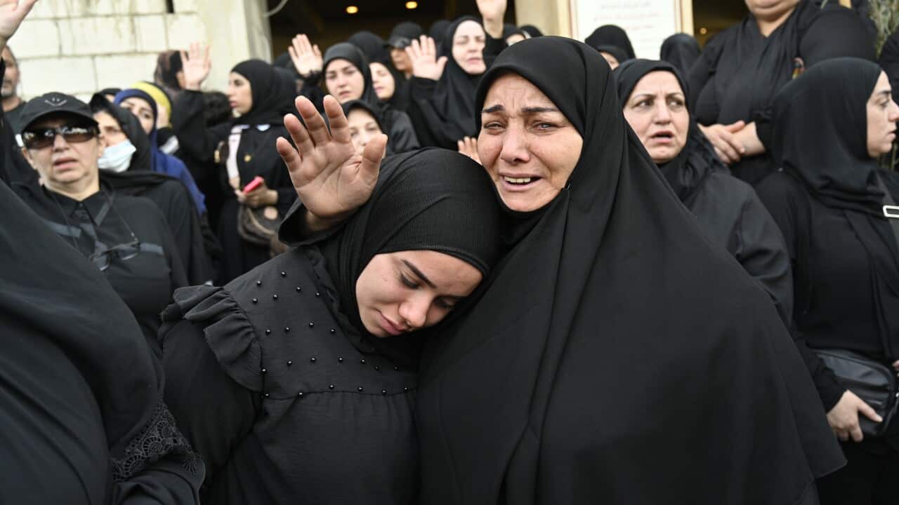 Two women in burqas are crying and hugging each other, surrounded by a group of women in burqas.