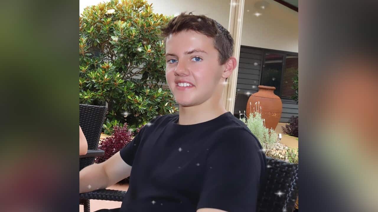 A photo of Jeremy Webb. He is sitting in a garden dressed in a black t-shirt, smiling at the camera.